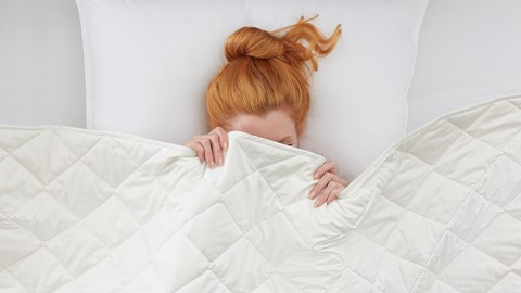Vrouw met rood oranje haar in bed met kussen en dekbed