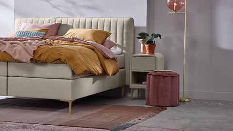een bed met een roze kleed en een roze krukje