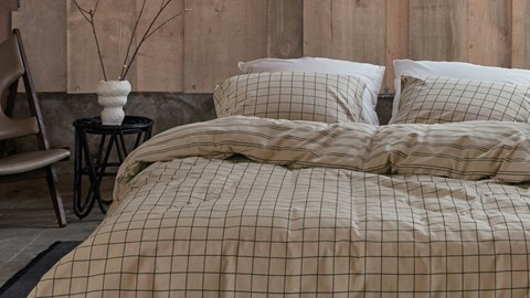 een bed met een witte vaas en een bruine muur