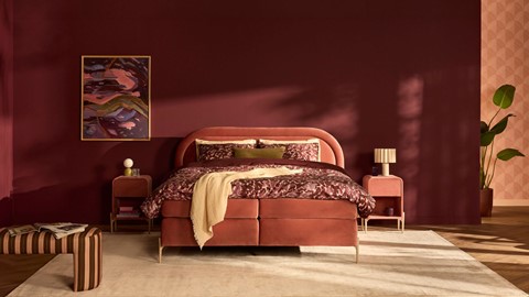 een bed met rood beddengoed en een schilderij aan de muur