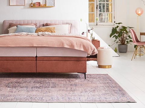 een bed met roze beddengoed en een kleed in een kamer
