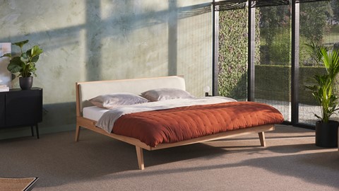 een bed met een rode deken en kussens in een kamer met een muur en planten