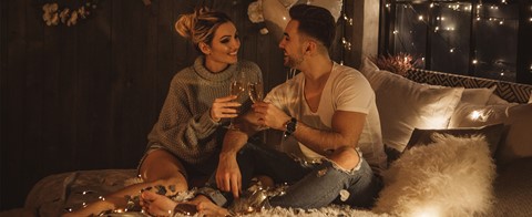 Een man en een vrouw die op een bed met wijnglazen zitten