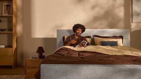 Een man die in bed ligt en een tijdschrift leest.