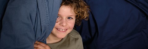 Een kind dat zich achter een blauwe deken glimlacht verbergt