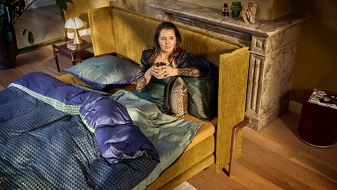 Vrouw zit met kop koffie op M line Element Vivid bed
