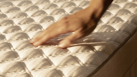 een hand die naar de bovenkant van een matras reikt