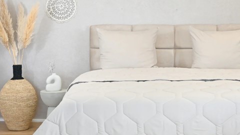 een bed met een witte deken en een witte vaas aan de zijkant