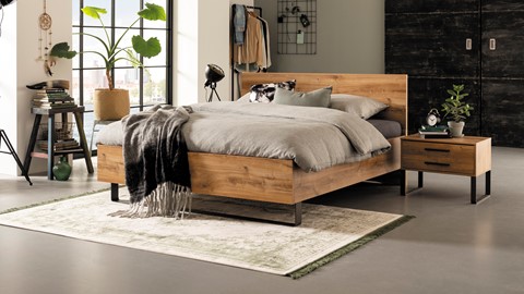 een bed met een deken en een kleed in een kamer met een raam