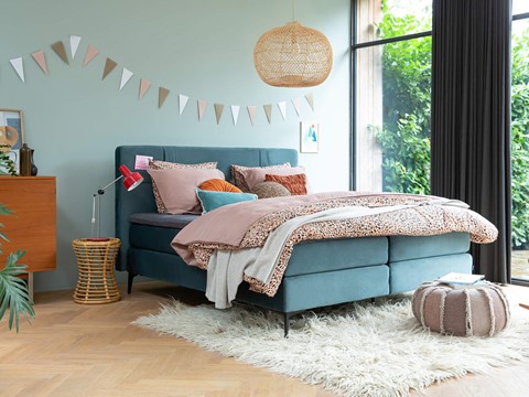 Blauwe boxspring met rotan lamp en nachtkastje