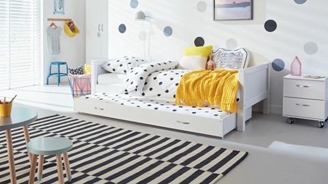 Een wit bed met zwarte stippen en gele deken