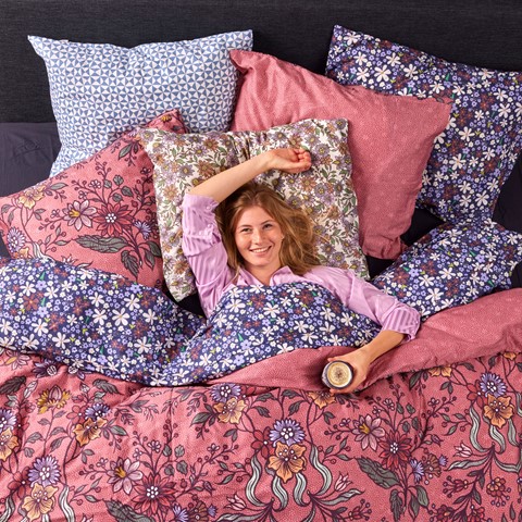 Vrouw in bed met roze bloemen dekbedovertrek en veel kussens