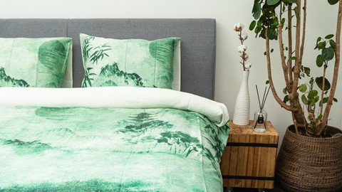 een bed met een groen dekbed en een plant in een vaas