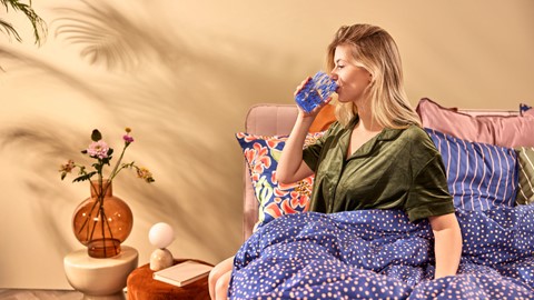 Een vrouw die in een stoel zit te drinken uit een blauw glas