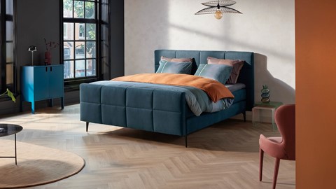 een blauw bed met oranje kussens en een lamp