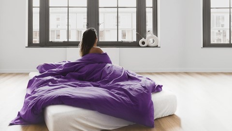Vrouw zit op Wave matras met paarse deken om zich heen
