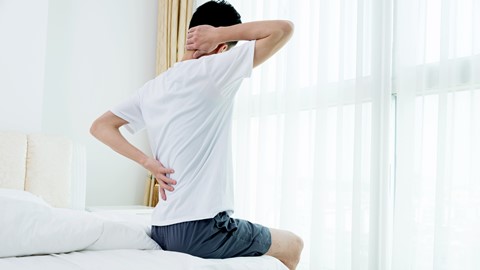 Een man zittend op een bed met zijn rugpijn