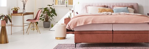 Een bed met roze deken en kussens in een kamer met een plant