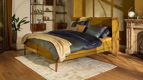 Een okergeel bed met kleurrijk beddengoed