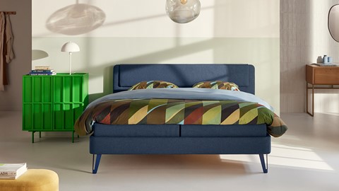 een bed met een kleurrijk beddengoed en een groen nachtkastje