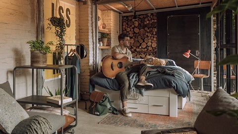 Een man die op een bed zit en een gitaar speelt